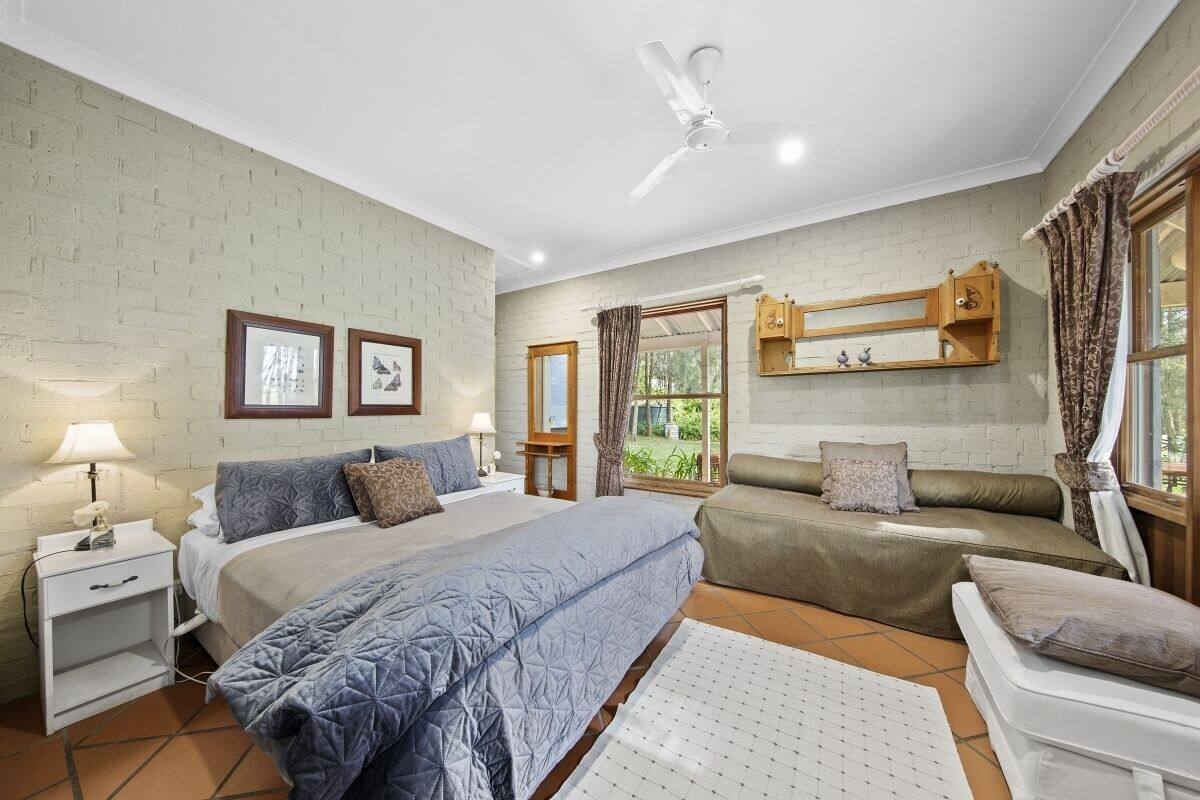 A bedroom with a bed, bedside tables, a ceiling fan, a window with curtains, and a wooden cabinet above the bed.