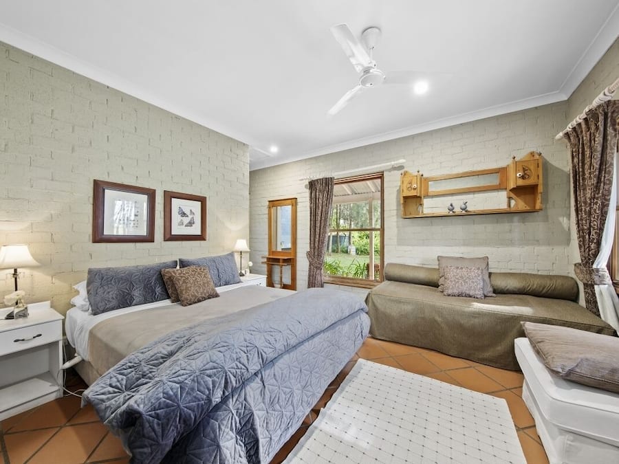 A bedroom with a bed, bedside tables, a ceiling fan, a window with curtains, and a wooden cabinet above the bed.