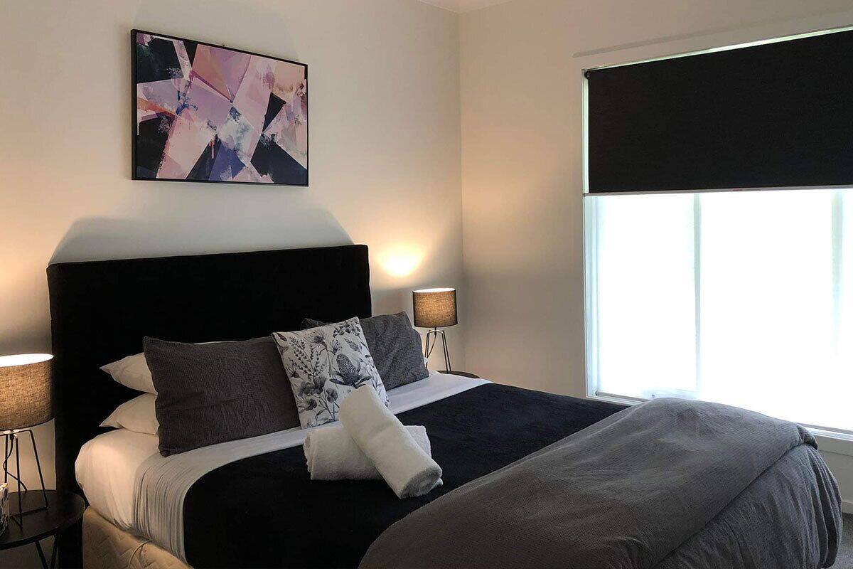 A neatly made bed with a black headboard, two bedside lamps, and a large abstract painting on the wall.