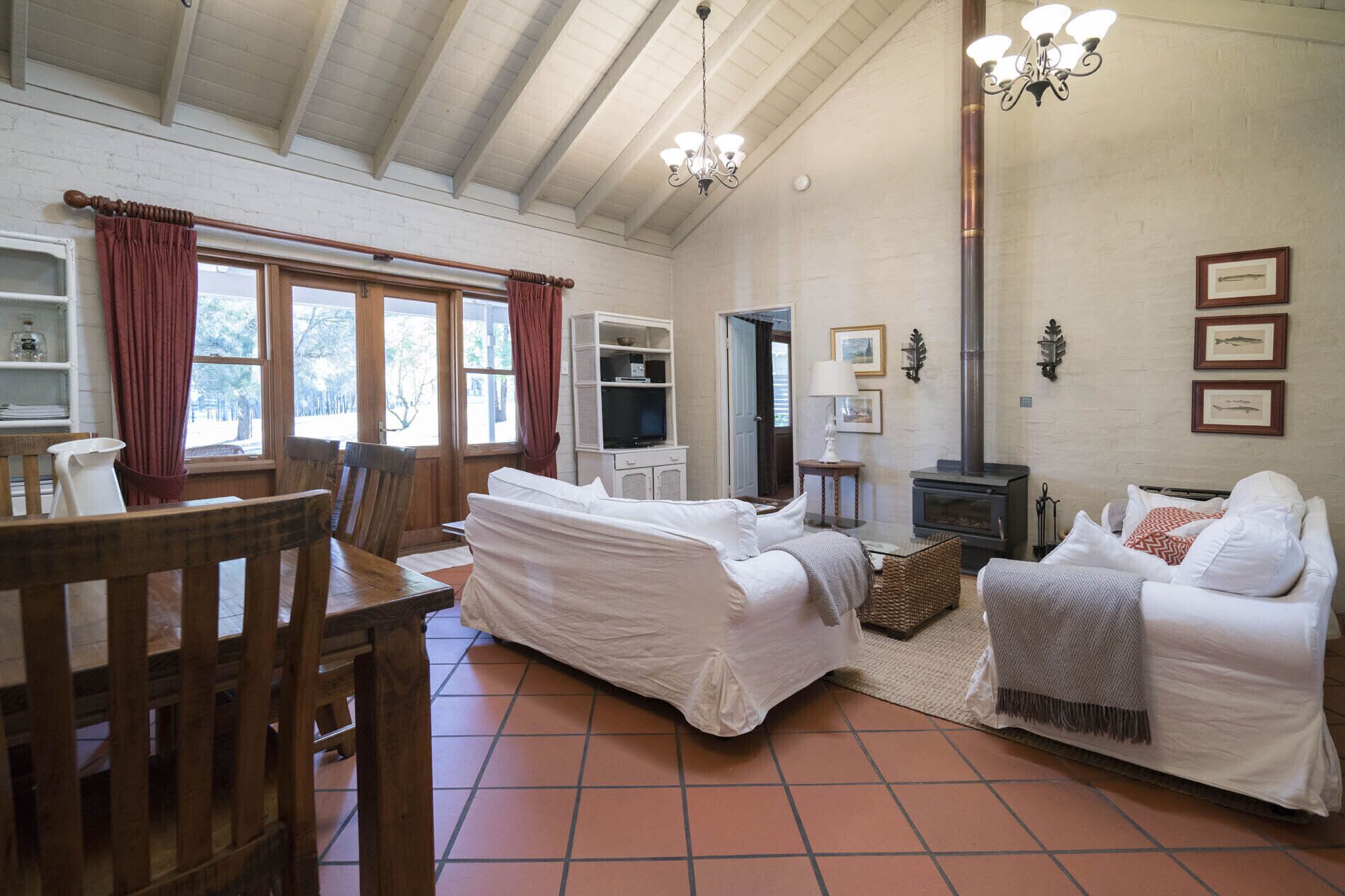 A cozy living room with a fireplace, a dining area with wooden furniture, and a large window with curtains.