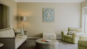 Una sala de estar con sofá, sillón, reposapiés y lámpara.