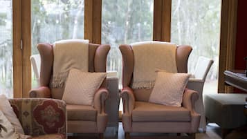 Una habitación con dos sillones a rayas con almohadones, un sofá estampado y vistas a árboles a través de amplias ventanas.