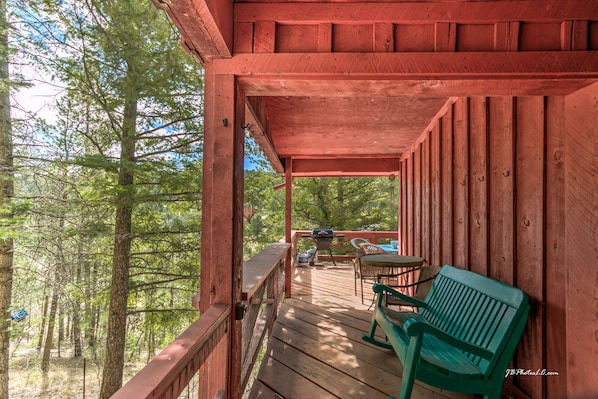 Une terrasse en bois avec une rambarde rouge, un banc vert et une table avec des chaises.