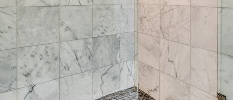 Un baño moderno con paredes de mármol, ducha con cabezal de lluvia y piso con diseño de guijarros.
