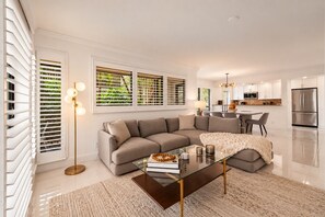 A modern living room with a sectional sofa, a glass coffee table, and a kitchen in the background. - PGA National Private Entrance Condo W/ Amazing Golf Course Views-2023 Renovation (Palm Beach Gardens)