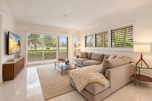 A modern living room with a beige sofa, a glass coffee table, and a TV on the wall.