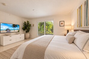 A bedroom with a bed, a TV, a plant, and a window with blinds.