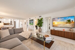 A modern living room with a sofa, coffee table, and a TV displaying a beach scene.