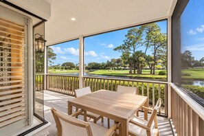 Un balcón con una mesa y sillas de madera, con vistas a un campo de golf.