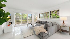 A modern living room with a grey sofa, a glass coffee table, and a white side table.