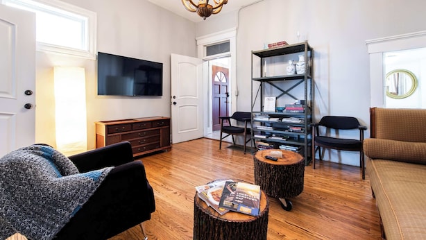 Ein Wohnzimmer mit Fernseher, Holzboden, einer Deckenleuchte, einem Bücherregal und einem Sofa.