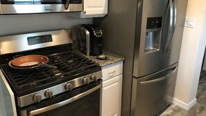 Een keuken met een gasfornuis, oven, een roestvrijstalen koelkast, magnetron en koffiezetapparaat.