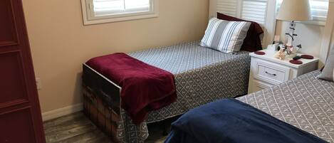 A bedroom with two beds, a dresser, a nightstand, and a lamp.
