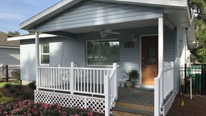 Eenlaags huis met een overdekte veranda, een voordeur en een kleine tuin met roze bloemen.