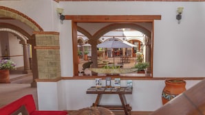 Un rincón interior acogedor con un sofá rojo, una mesita con folletos y vistas a un patio exterior con sombrillas y plantas.