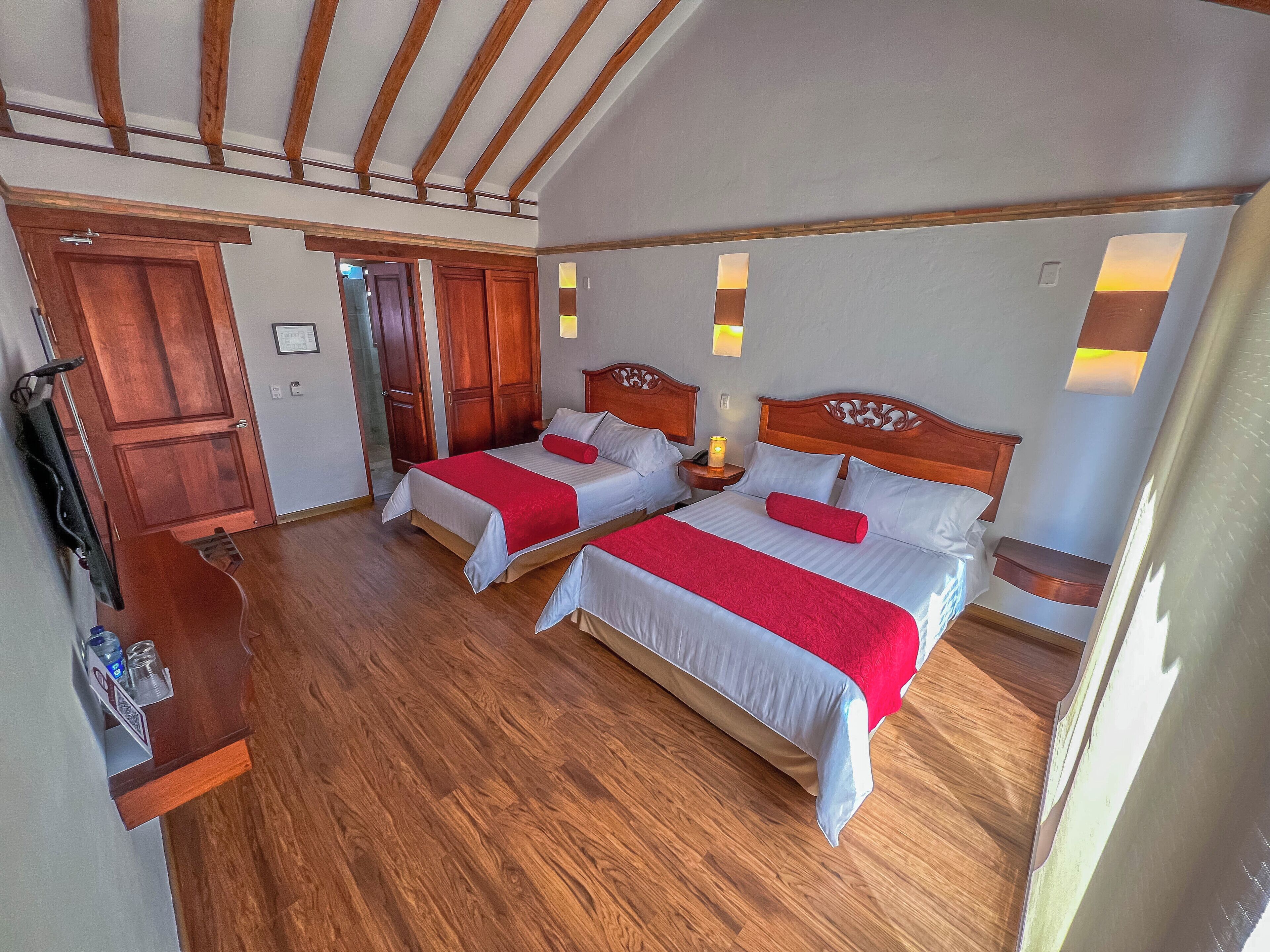 Ett hotellrum med två sängar, trägolv och ett tak med synliga takbjälkar.