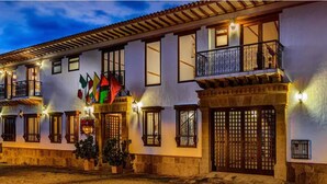 Un edificio de varios pisos con balcones, una puerta de madera grande y varias ventanas. Se ven banderas frente al edificio.