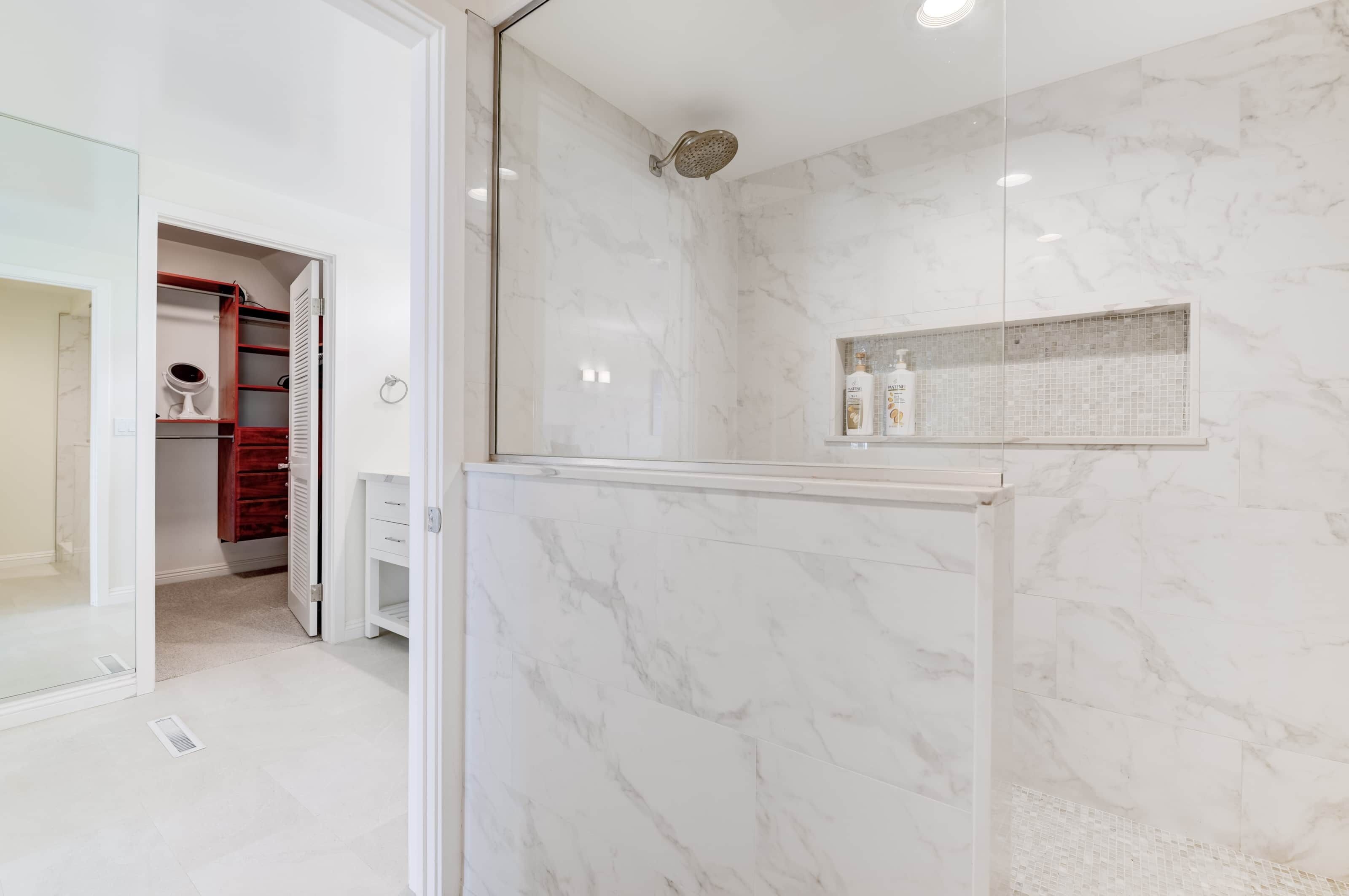 Une salle de bain moderne avec une douche à parois de verre, des murs en marbre et un meuble-lavabo avec des articles de toilette.