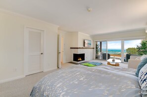 Une chambre à coucher avec un grand lit, une cheminée, un balcon avec vue et une porte donnant sur une autre pièce.