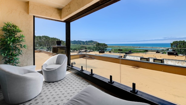 Varanda com vista para a praia e oceano, com um sofá e um vaso de planta.