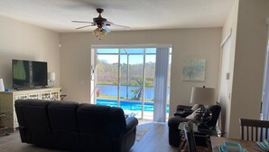 A living room with a black sofa, a television, and a dining table with blue plates. - Exec. 4 Bedroom Home nr Disney,   Backs onto Conservation lands (Kissimmee)
