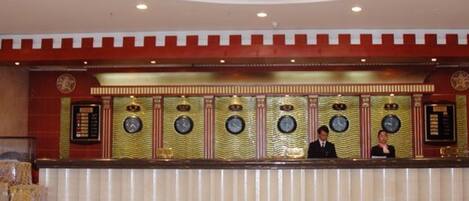 A hotel reception area with a large chandelier, a reception desk, and multiple clocks on the wall.