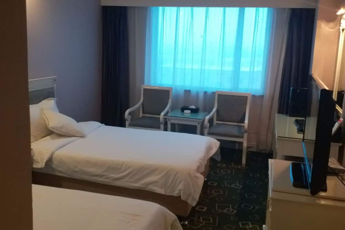 Ein Hotelzimmer mit zwei Betten, einem Schreibtisch, einem Sessel und einem Fernseher.