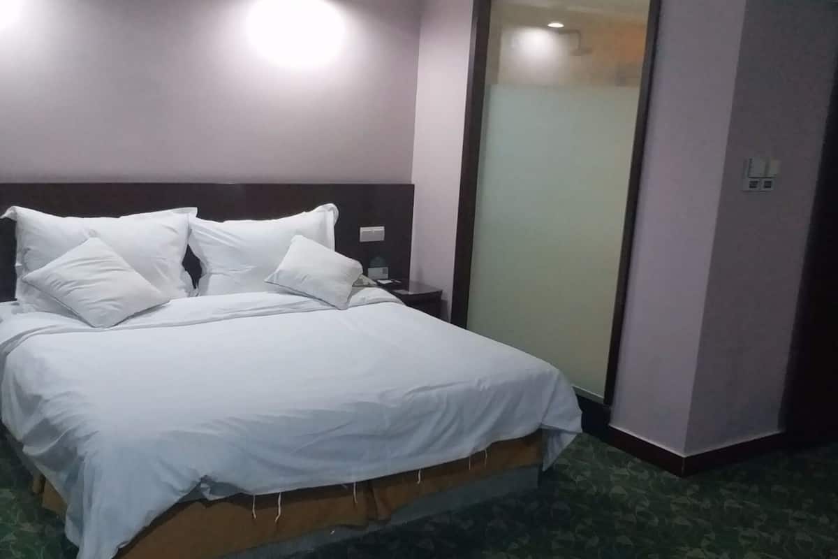 Ein ordentlich bezogenes Bett mit weißen Leinentüchern in einem Hotelzimmer mit gemustertem Teppich.