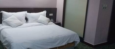 Una cama bien tendida con sábanas blancas en una habitación de hotel con alfombra estampada.
