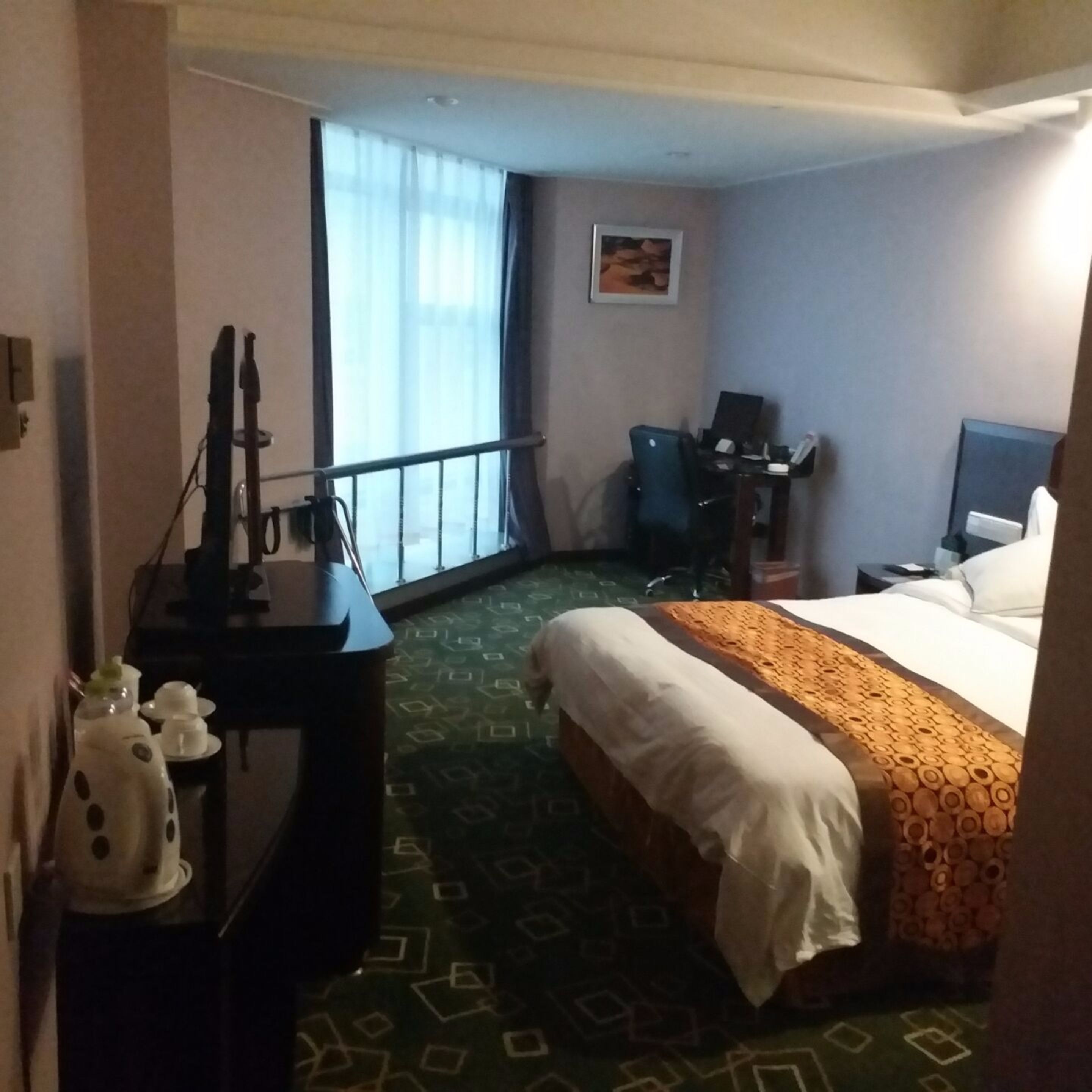 A hotel room with a bed, a desk, a chair, and a window with curtains.
