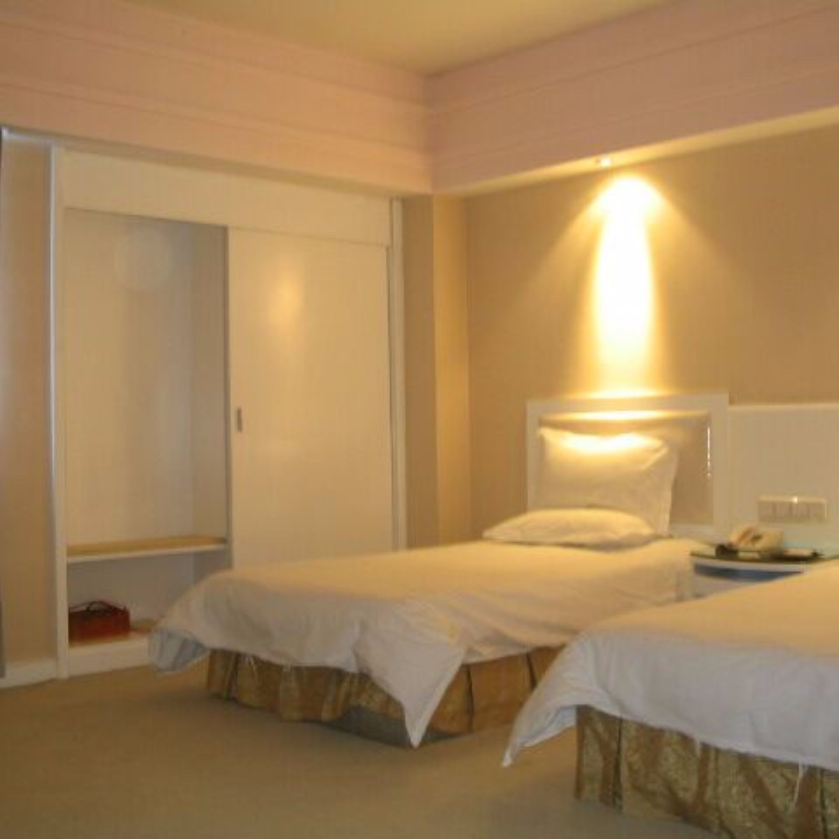 Habitación de hotel con dos camas, un armario y una mesita de noche con lámpara.