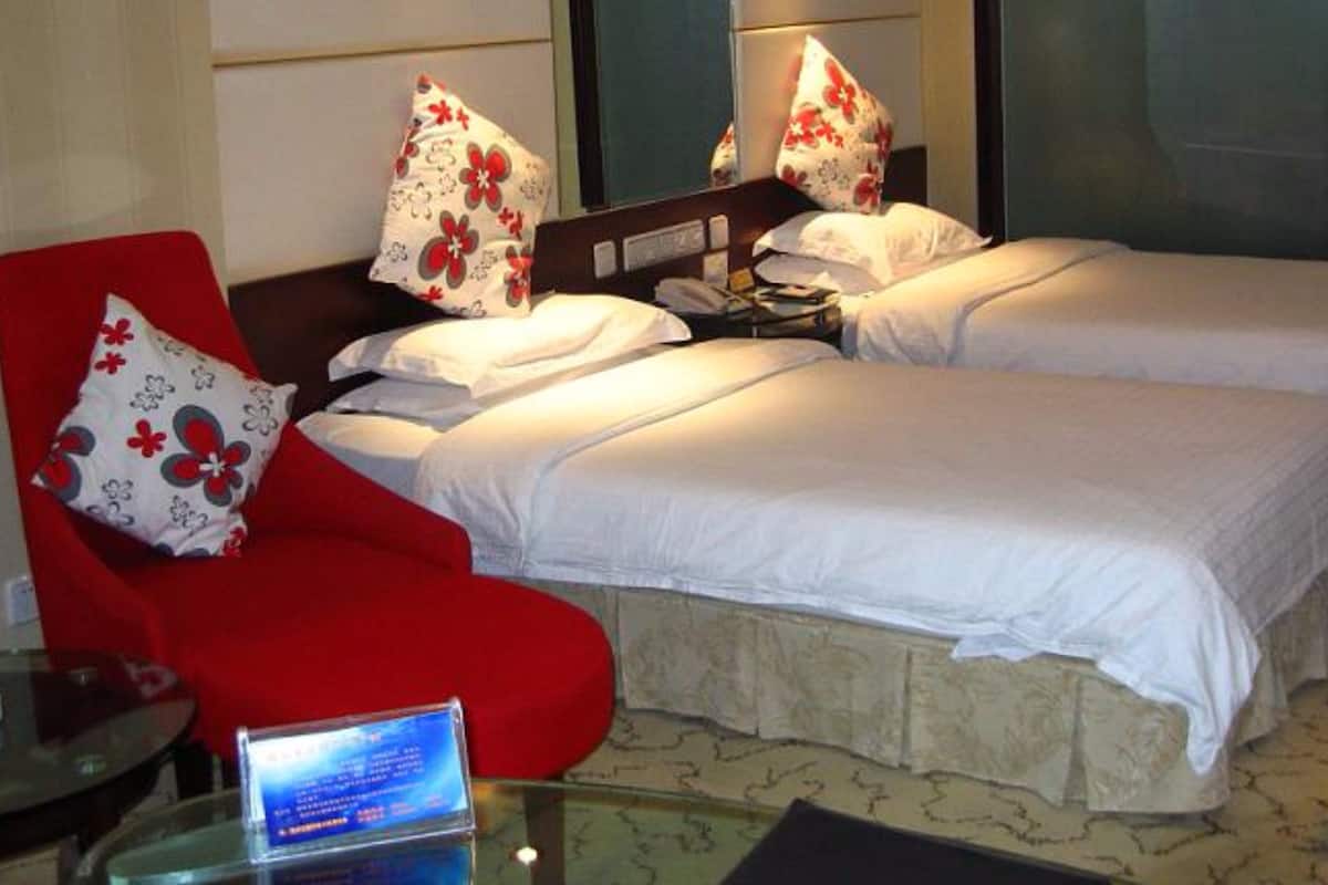 Ein Hotelzimmer mit zwei Betten, einem roten Sessel und einem Nachttisch mit einer Lampe.