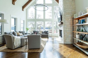 Un salón amplio con un gran ventanal, chimenea y suelo de madera.