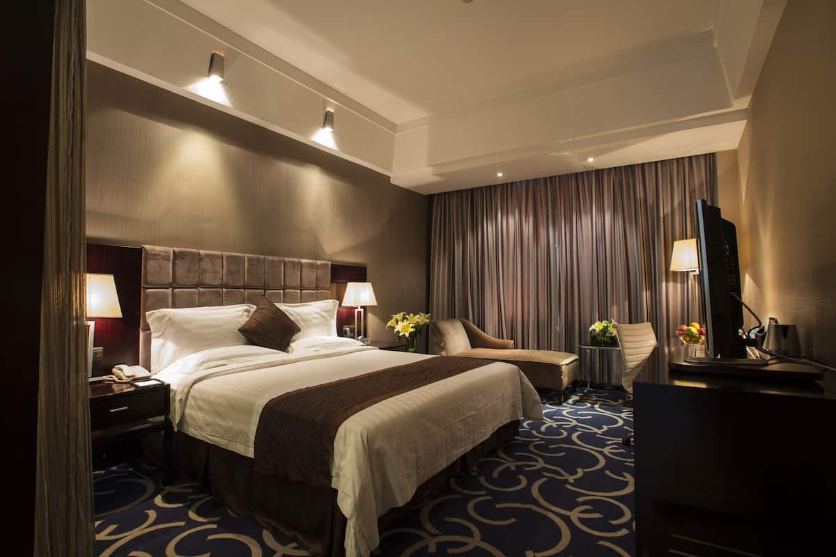 Ein Hotelzimmer mit einem großen Bett, einem Schreibtisch, einem Stuhl, einem Fernseher und einer Lampe.