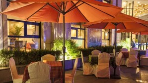 An outdoor seating area with tables and chairs, covered by large umbrellas, and a building with windows in the background. - Yinchuan Vintage Hill Hotels & Resorts (Yinchuan)