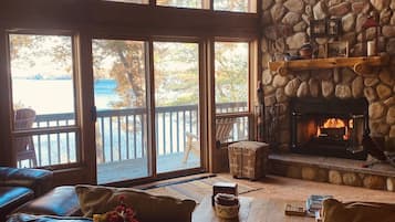 A cozy living room with a stone fireplace, leather sofas, and a large window overlooking a deck.