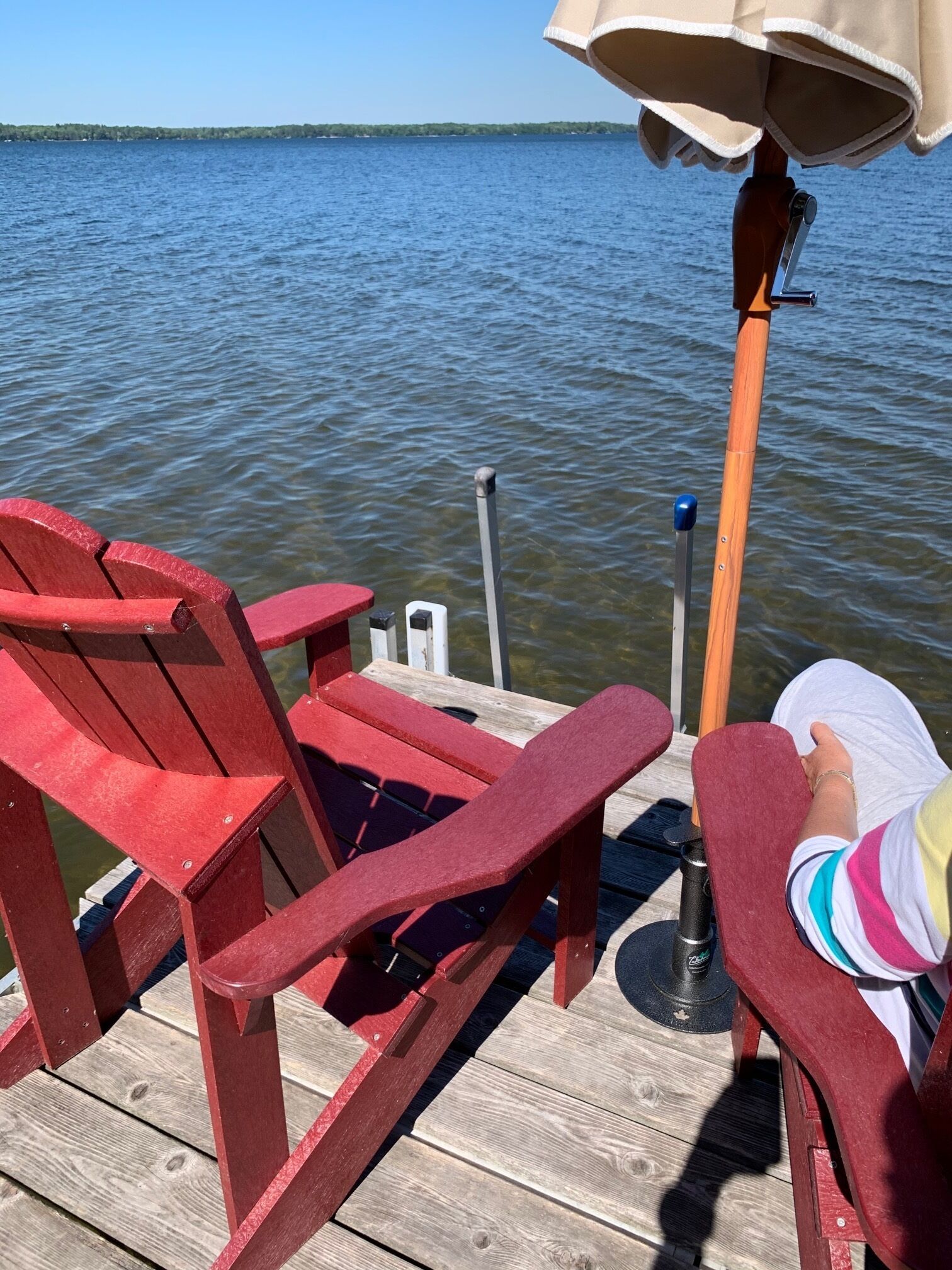 A wooden deck with red Adirondack chairs, a small table, and a lamp.