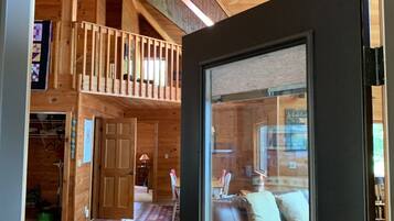 A wooden interior with a 'WELCOME' sign, a staircase, a dining area, and a living room with a pink sofa.