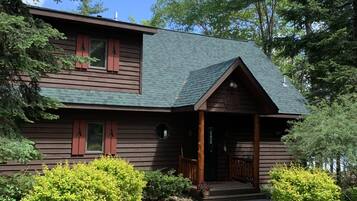 A two-story log cabin with a green roof, a front porch, and a stone pathway leading to the entrance.