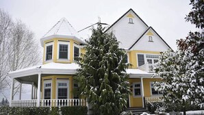 Une maison à deux étages, dotée d’une tourelle d’angle remarquable et d’un grand arbre à feuilles persistantes devant.