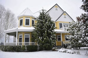 A two-story house with a prominent corner turret and a large evergreen tree in front.