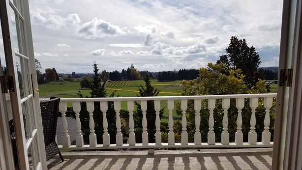 Un balcon doté d’une balustrade blanche, donnant sur un jardin aménagé et sur des champs situés au loin.