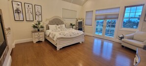 Une chambre à coucher avec un grand lit, une table de chevet, une commode et une fenêtre donnant sur les arbres.
