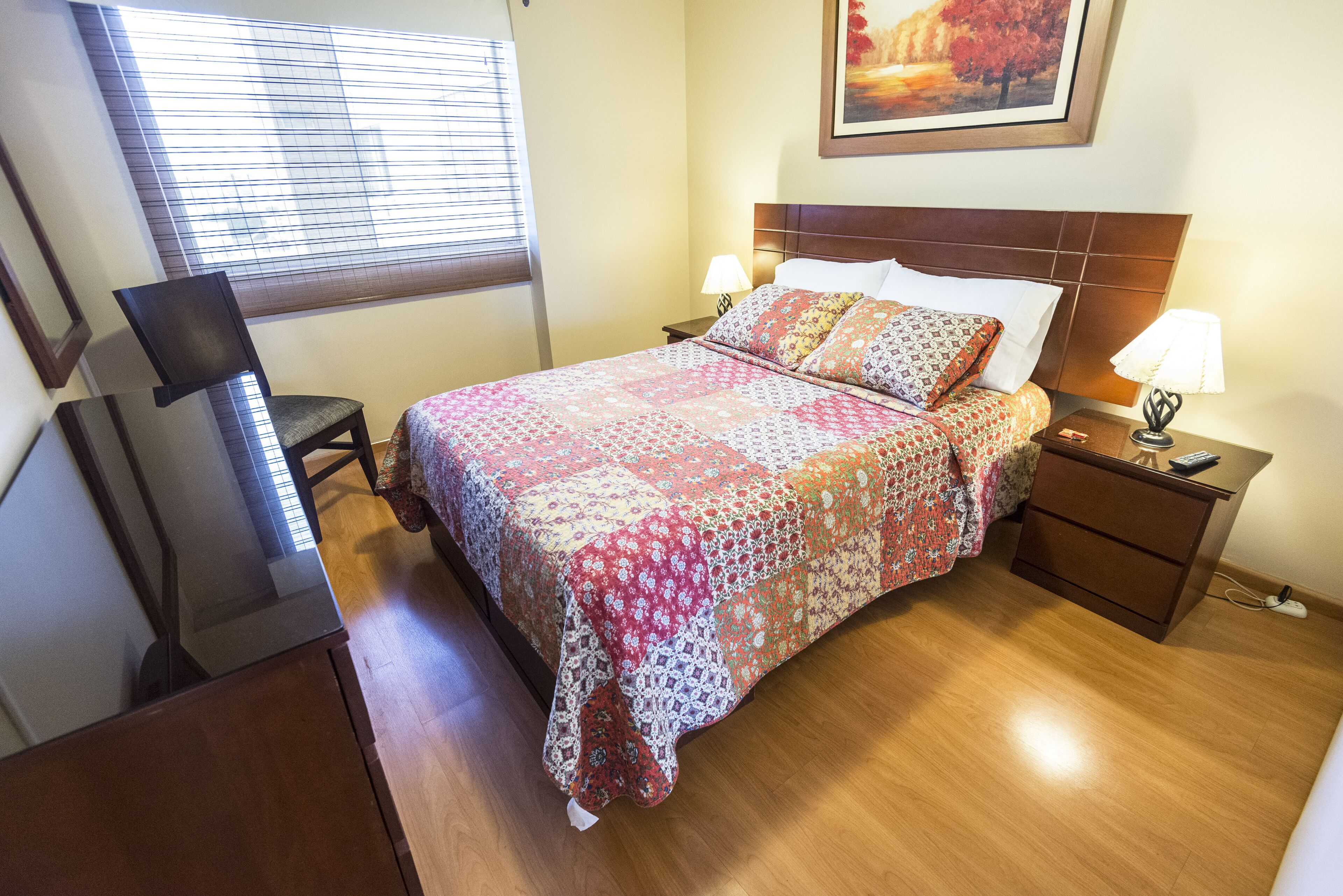 A neatly arranged bedroom with a bed, bedside tables, a desk, and a chair.