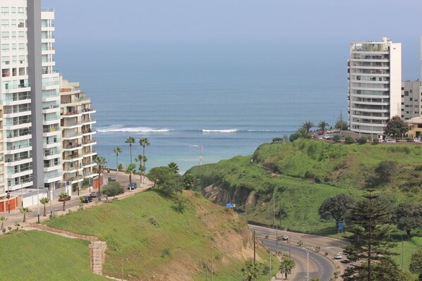 A coastal cityscape with high-rise buildings, a curved road, and a view of the ocean. - OCEAN VIEW SPECTACULAR & ROMANTIC WALK IN FRONT LARCOMAR/QUEBRADA DE ARMENDARIZ (Miraflores)