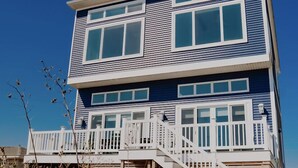 Uma casa de praia térrea com varanda branca e escada que leva à entrada.