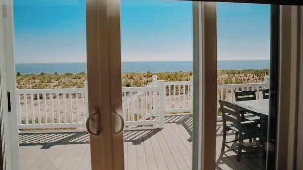 Vista de um quarto com porta de vidro deslizante para um deck com cerca branca e mesa com cadeiras.
