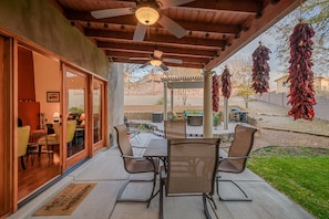 A covered patio with a table and chairs, a ceiling fan, and hanging dried chilies.