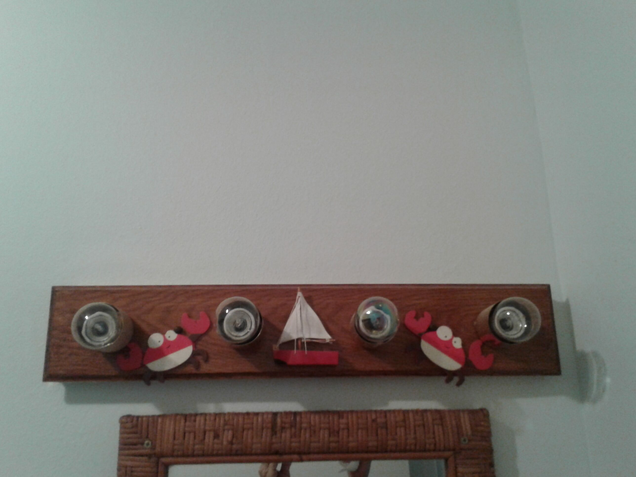 Une étagère en bois fixée au mur, ornée de quatre objets ronds, d’un petit voilier et de deux décorations représentant des crabes rouges.