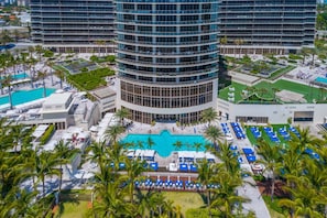 A modern hotel with a central swimming pool, multiple balconies, and lush landscaping.